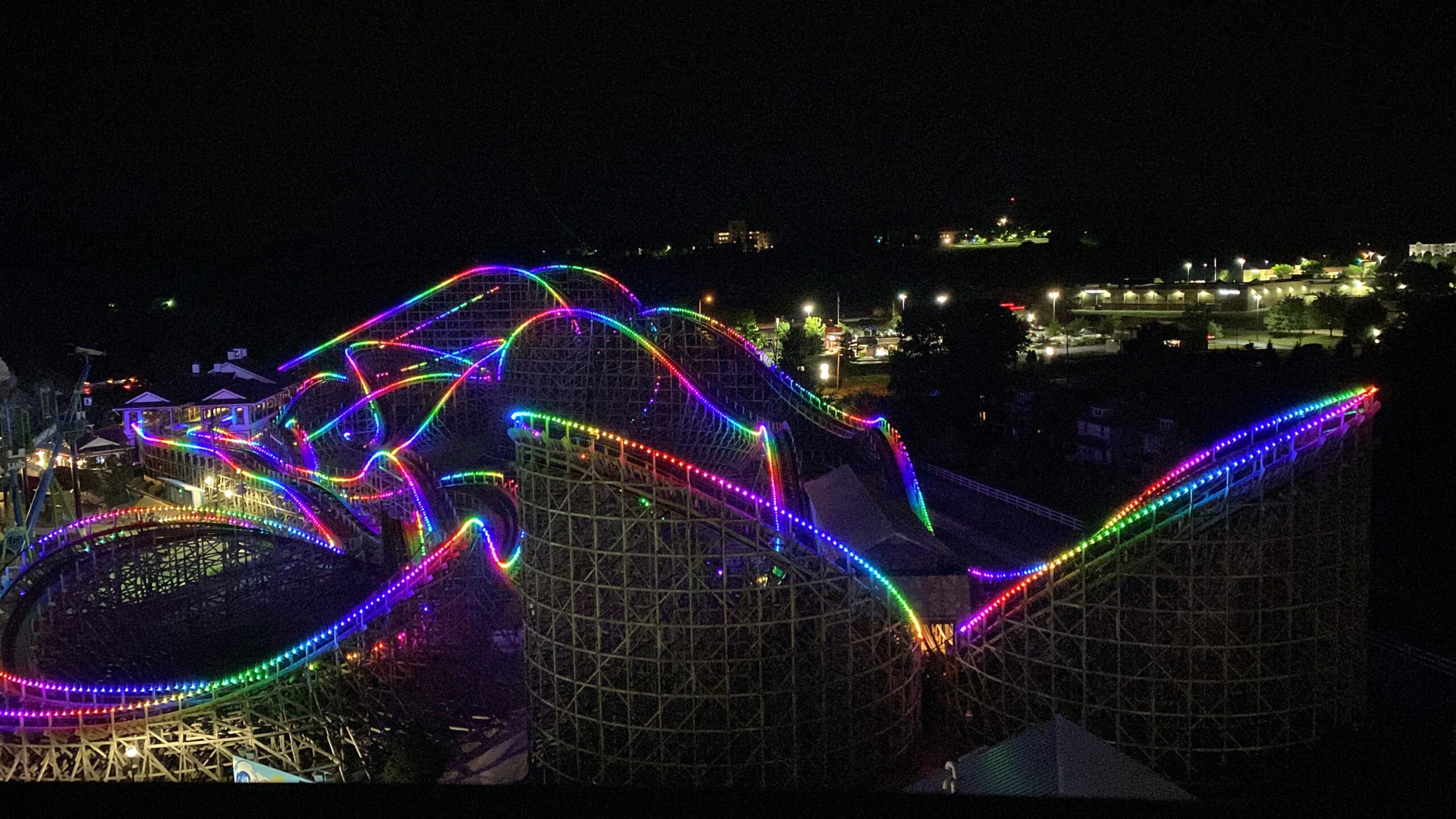 A Large Roller Coaster At Night Lit Up With Neon Lights.